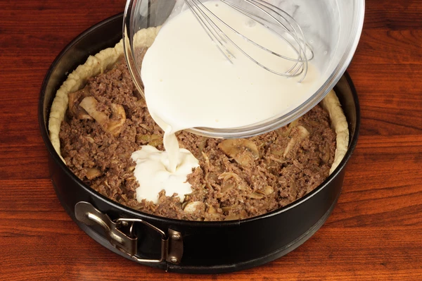 Собрать киш: для этого в форму выложить подготовленный фарш, залить сливочной смесью.