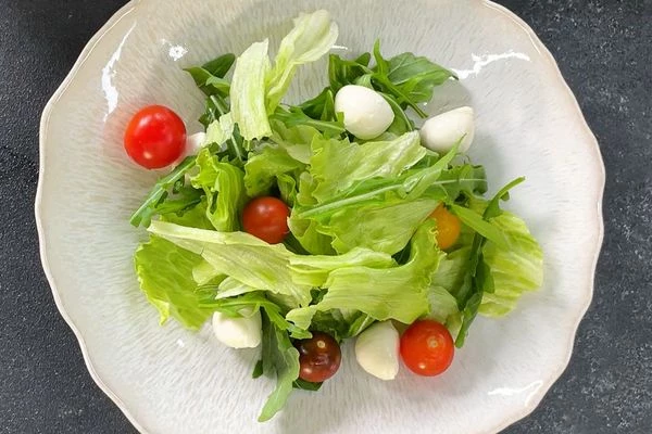 В тарелку для подачи выложить листья салата, помидоры черри, моцареллу.


