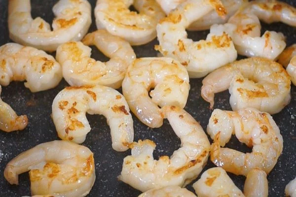 Креветки разморозить на нижней полке холодильника. Ножом с внутренней стороны сделать надрезы, не перерезая креветку. Немного креветок оставить без надрезов - для оформления. 
В сковороду налить оливковое масло, добавить раздавленный зубчик чеснока, обжарить все креветки, посолить.
