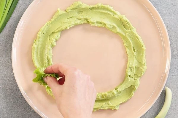Соус из авокадо распределить по круглой тарелке, чтобы получилось кольцо. На соус выложить салатные листья. 
