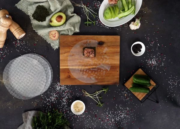 Выложить бумагу на доску. На нее с краю по центру выложить кусочек нори, сверху обжаренный тунец.