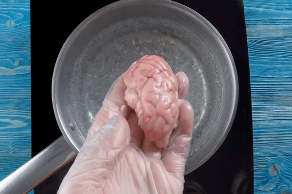 Мозги разморозить естественным способом, промыть под холодной водой. В кастрюле воду довести до кипения, проварить мозги 5-7 минут. 