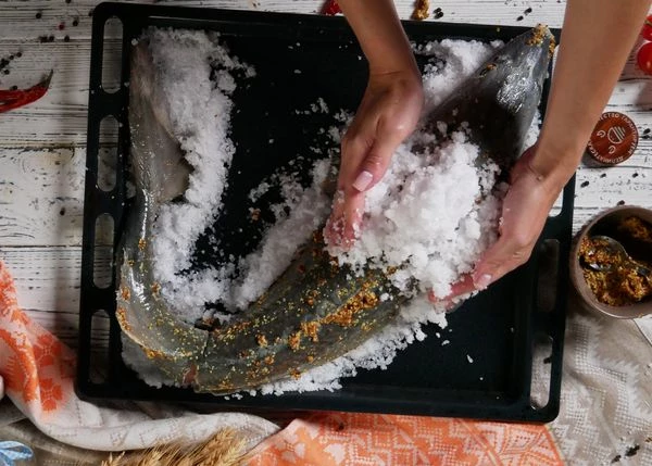 Насыпать на противень слой соли толщиной, примерно, 1 сантиметр. Положить рыбу брюшком вниз, смазать оливковым маслом, выложить оставшуюся соль сверху.