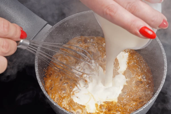 Влить к растопленному сахару сливки, быстро перемешивая венчиком карамель. Будьте осторожны, при вливании сливок, карамель резко поднимается вверх.