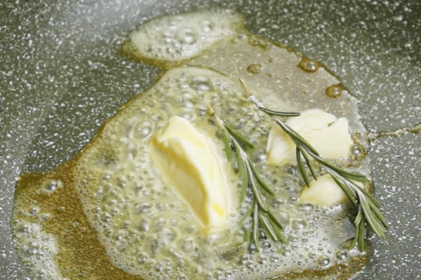 На сковороде разогреть сливочное масло, добавить раздавленные зубчики чеснока и веточку розмарина.