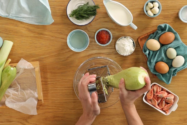 Подготовить кабачки. Вымыть и насухо вытереть. У молодых кабачков срезать кончики. Если кабачок старый, то надо обязательно очистить его от толстой шкурки и удалить из него семена. Натереть кабачок на крупной терке. 
Чеснок натереть на мелкой терке.
