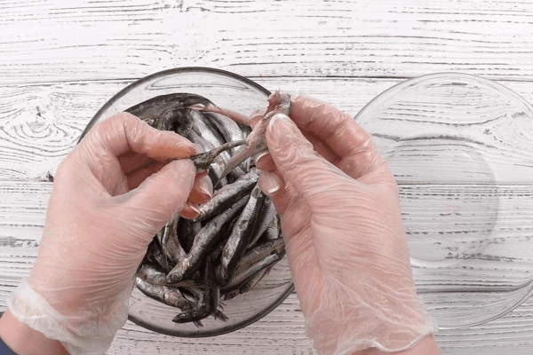 Рыбу разморозить естественным способом на нижней полке холодильника, промыть под холодной водой (если есть поломанные рыбки — не страшно, для тушения они тоже подойдут). Удалить голову с кишечником (руками, как мы, или с помощью ножа: сделать надрез над головой со стороны спинки и потянуть — внутренности вытянутся вместе с головой).