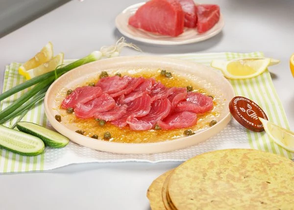 Выложить слайсы тунца. Огурцы очистить от кожуры, нарезать тонкими кружочками. Выложить на тунца. 