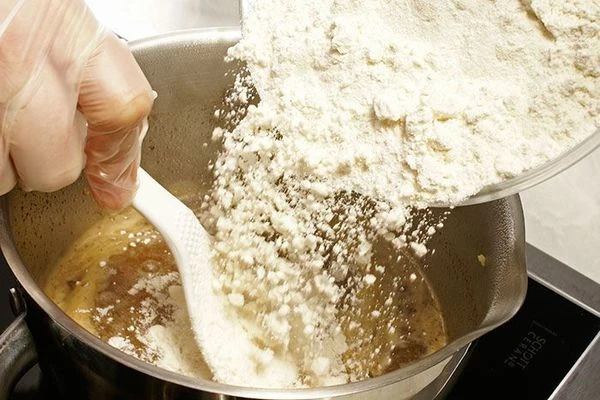 Довести до кипения, всыпать 1/2 часть муки и быстро замесить однородное тесто без комочков.