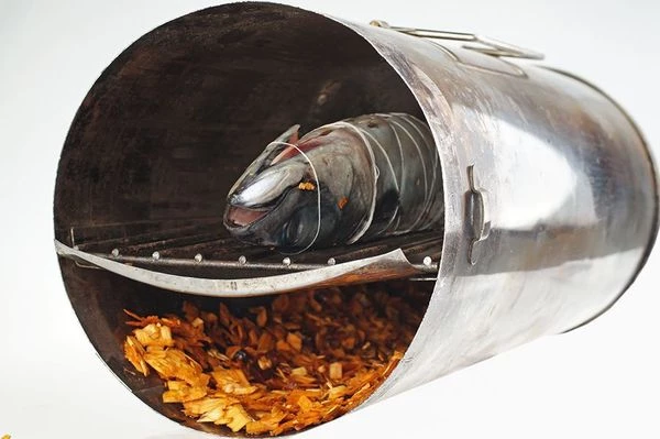 Выложить на дно коптильни опилки ровным слоем 1-1,5 см. Сверху установить поддон для стекания жира, над ним положить решетку с рыбой. Закрыть крышку коптильни.