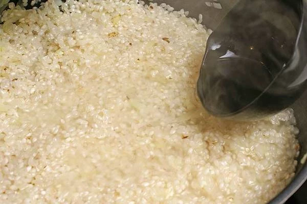 Приготовить бульон для ризотто, оставить сбоку на плите, чтобы он постоянно был горячим. Как только вино выпарится, вливать небольшими половниками бульон, аккуратно перемешивая рис, чтобы не поломать структуру зерен. Не рекомендуется заливать рис более, чем на 0,5 см сверху.