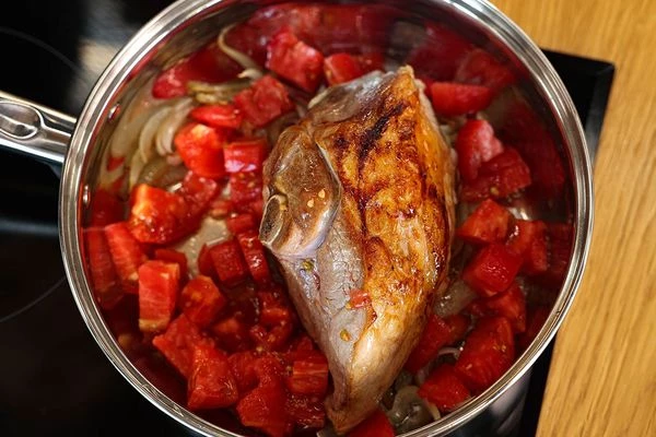 В глубокую сковороду с толстым дном выложить обжаренный лук, окорок, нарезанные томаты, посолить, поперчить, влить половину воды.
Закрыть крышкой и томить на медленном огне около 45-50 минут, пока мясо не станет совсем мягким. Постепенно доливая оставшийся бульон или воду.
