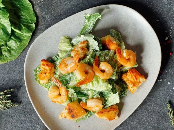 Выложить на порционную тарелку листья салата, сверху положить креветки и гренки из багета.