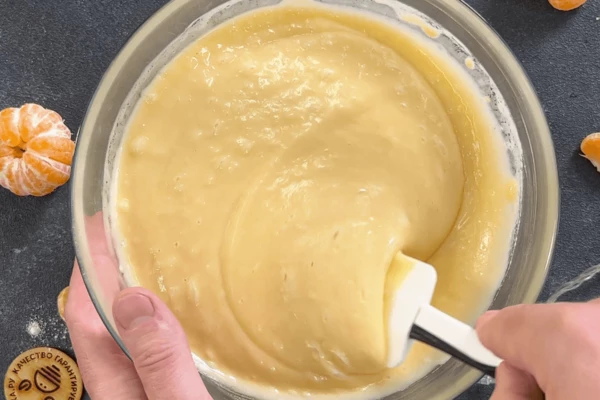 К смеси мандаринов и яиц добавить сахар, щепотку соли, масло подсолнечное и воду. Просеять муку с разрыхлителем и тщательно перемешать.