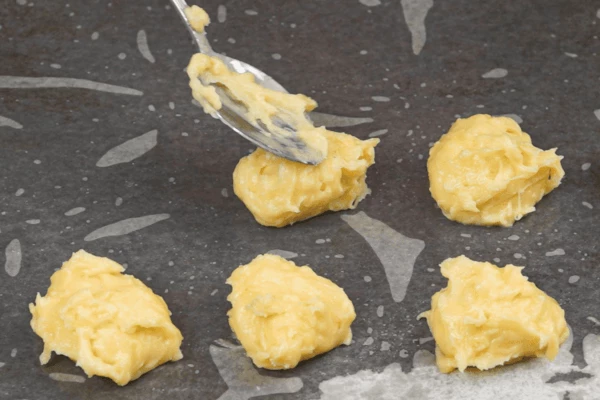 Готовое тесто с помощью ложки переложить на застеленный пергаментом противень в виде шариков, примерно на расстоянии 2 см друг от друга. 