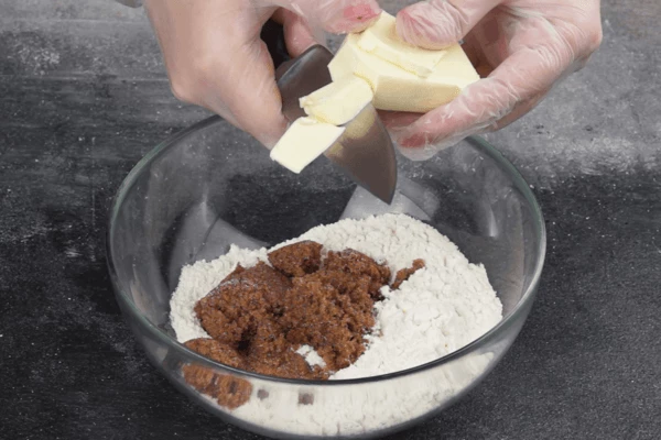 Приготовить крамбл: холодное масло (115 г) нарезать кубиками, смешать с мукой и сахаром, перетереть в крупную крошку.