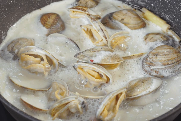 Вонголе промыть под проточной водой. В сковороду выложить моллюсков, снова довести до кипения и варить, пока моллюски полностью не раскроются, от 5 до 8 минут.
