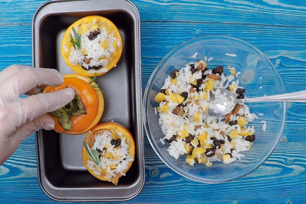 Зафаршировать хурму рисом с сухофруктами, украсить веточками розмарина. Выложить в форму для запекания. 