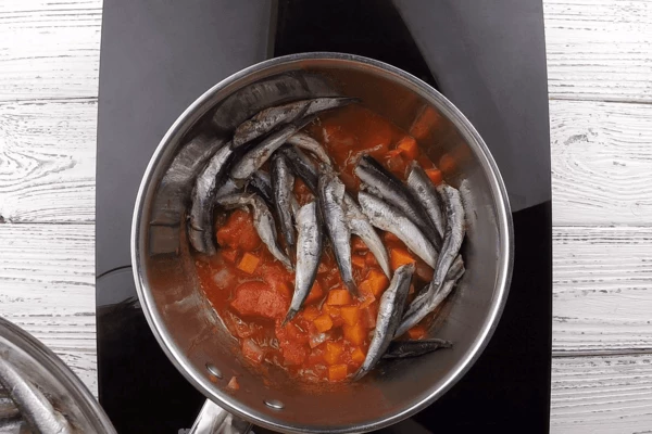 В кастрюлю с высокими бортами выложить часть овощной заправки, затем рыбу.