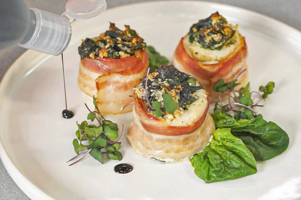 Готовые рулеты переложить на тарелку для подачи. Оформить шпинатом, микрозеленью и каплями бальзамика.