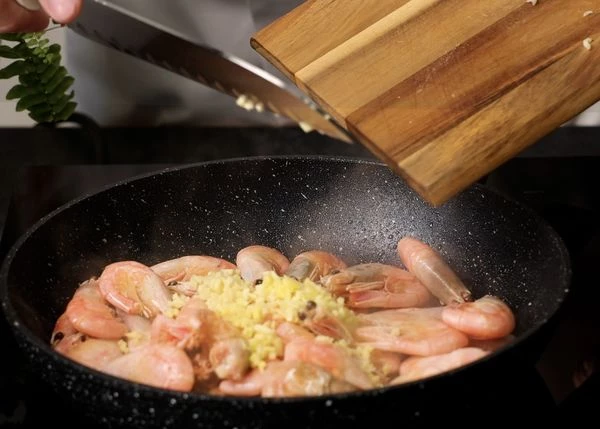 Креветки разморозить. Нагреть сковороду и влить в нее растительное масло. Выложить креветки, нарезанный имбирь и чеснок. Обжарить 1 минуту на высоком огне.   