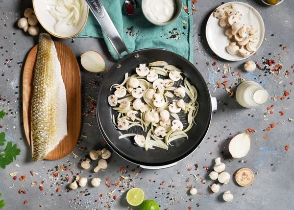 Лук очистить, нарезать перьями. Шампиньоны вымыть, разрезать пополам.
На оливковом масле обжарить лук и шампиньоны в течение 1,5 минут. 
