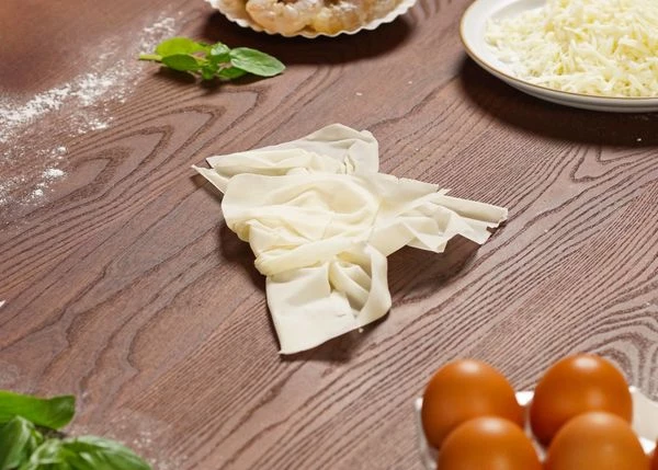 Сложить тесто крестом, сминая тесто с каждой стороны от края к центру. У полученного креста сложить одну часть в середину. 