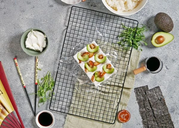 Рис отварить, как для суши, добавить заправку, перемешать, дать полностью остыть. 
Авокадо вымыть, очистить, нарезать слайсами. 
Лоток для яиц застелить пищевой пленкой. На дно каждой ячейки выложить ломтик угря и авокадо.
