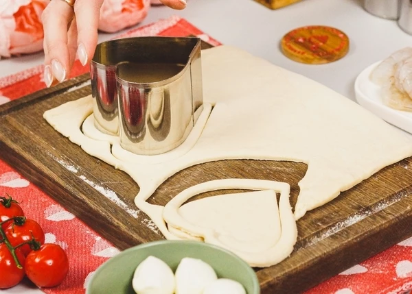 Тесто разморозить, немного раскатать на припыленной мукой доске. С помощью форм вырезать сердечки. 