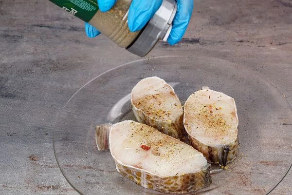 Стейки трески разморозить естественным способом на нижней полке холодильника, обсушить бумажным полотенцем. Замариновать в небольшом количестве растительного масла и специй, оставить минут на 15.