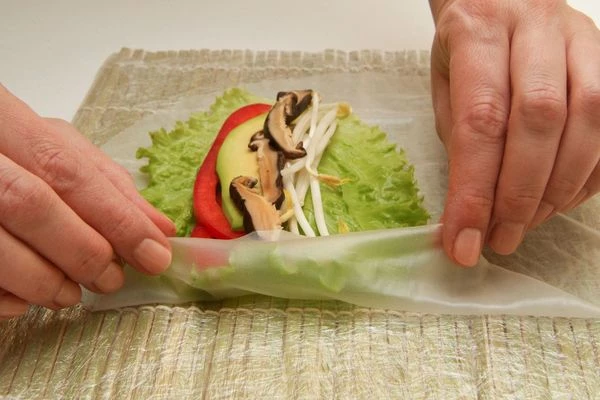 Выложить в центр листа начинку и накрыть ее краями рисовой бумаги.

