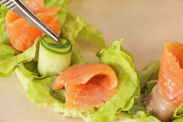 Слайсы огурца свернуть в трубочки ( розочки) и выложить на листья салата. Рядом выложить розочки из рыбы. 