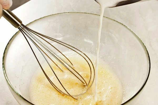 Влить тонкой струйкой горячее молоко к основной смеси, хорошо взбивая венчиком, чтобы желток не свернулся.