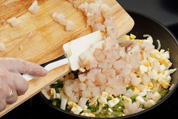 К луку добавить нарезанные вареные яйца и рыбу, посолить, поперчить по вкусу, перемешать.