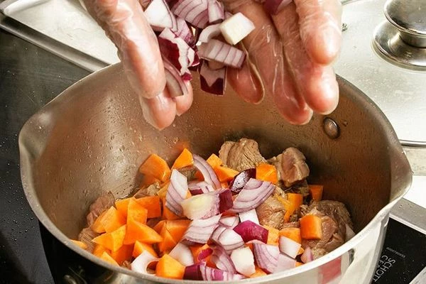 Обжарить в разогретой с оливковым маслом кастрюле мясо 10-15 минут, затем добавить нарезанные крупно морковь и лук.