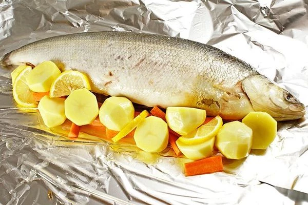 Вокруг зафаршированной тушки рыбы уложить овощи, дольки лимона, слегка посолить, поперчить.