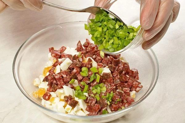 Смешать в отдельной чашке: вареные яйца, колбасу, лук зеленый.