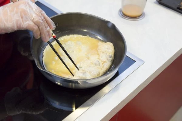 С одной стороны положите брусочки угря по всей длине. Затем, не пережаривая омлет, начинайте заворачивать в рулет с помощью палочек или лопатки.