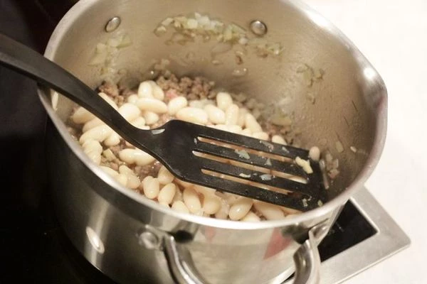 В разогретой кастрюльке на оливковом масле обжарить лук и чеснок, примерно 4 минуты, затем добавить фарш. Уменьшить огонь и готовить 5-6 минут, размешивая и убирая комки.