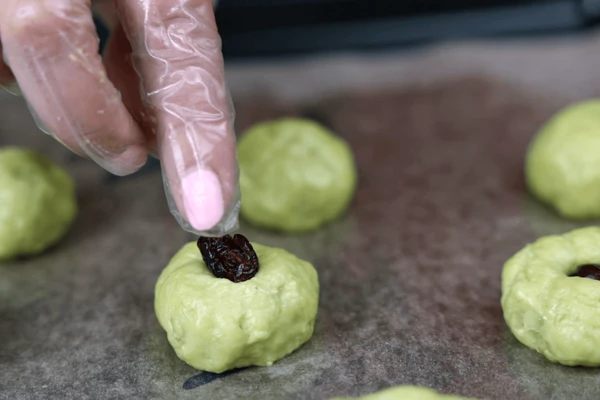 На смазанный пергамент выложить шарики из теста, в центр положить сушеную ягоду, придавить серединку. 