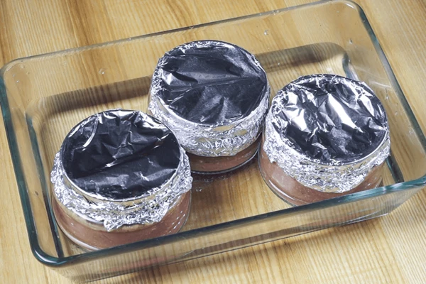 Закрыть плотно фольгой, поставить в форму, с водой (чтобы на ¼ часть закрывало баночки). Запекать в разогретой до 160С духовке 20-25 минут. Затем охладить до комнатной температуры