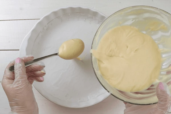 В форму для выпекания выложить промасленный пергамент по диаметру дна. Затем начинаем выкладывать тесто порциями. В центр выливаем ложку белого теста.