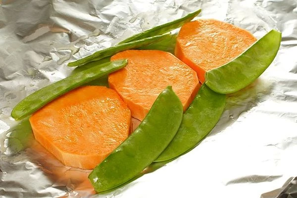 Лист фольги смазать маслом, выложить в центр нарезанный толстыми кружочками батат, рядом выложить лопатки зеленого горошка.