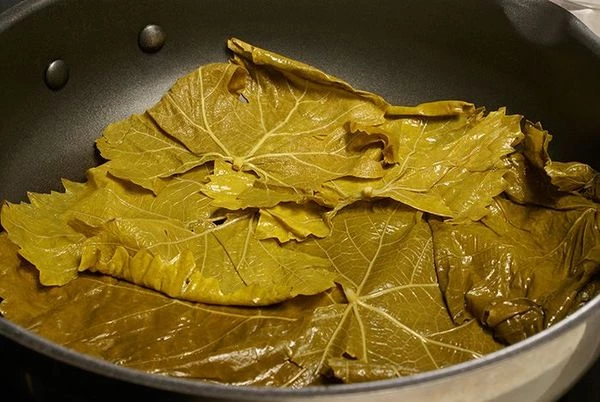На дно сковороды выложить слоем виноградные листья.