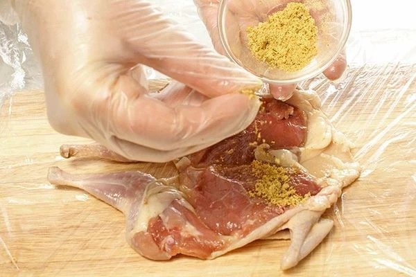 На доску расстелить пищевую пленку, на нее выложить филе перепела, посыпать специями и луком, нарезанным колечками.