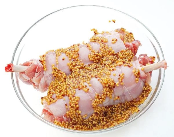 Мясо посолить, поперчить. Свернуть ножку кролика в плотный рулет, для вида можно вложить косточку. Обвязать кулинарной нитью. Замариновать в горчице на 10-15 минут.