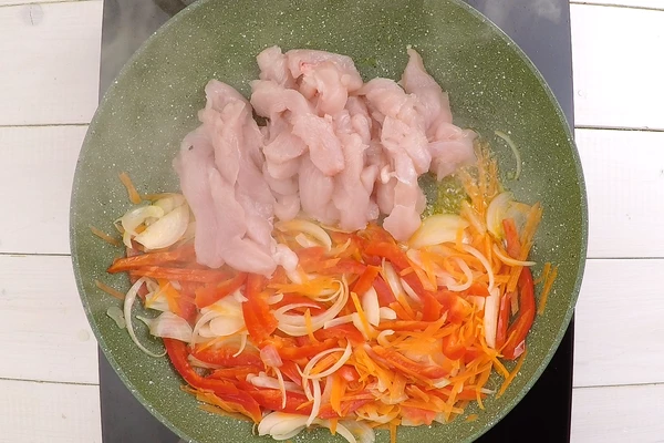 На разогретой с растительным маслом сковороде обжарить овощи, затем добавить куриное филе, жарить до полуготовности мяса. 