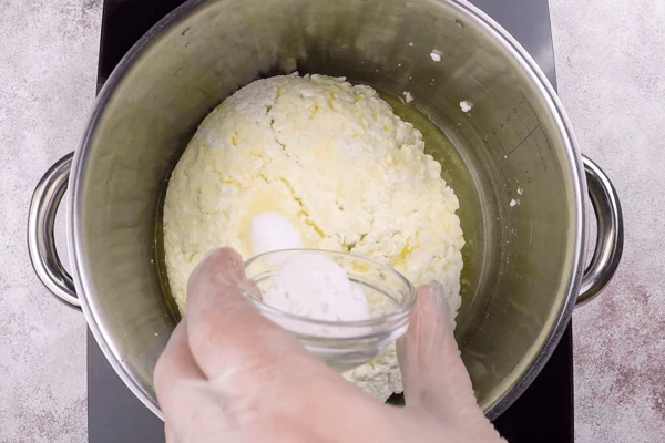 Переложить творожную массу в сотейник, добавить соль, соду и растопленное сливочное масло. Затем прогреть на водяной бане, постоянно помешивая, пока сыр не расплавится до однородной массы. 