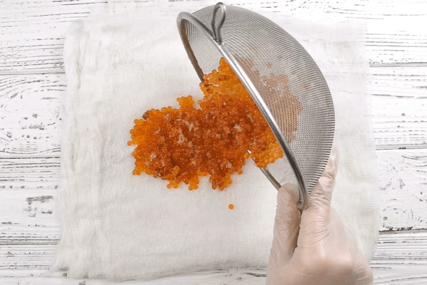  Раскрытые икринки сливаем через сито и перекладываем на несколько слоев марли или бумажное полотенце. 