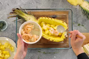 В запеченную половинку ананаса выложить кусочки нарезанного ананаса и обжаренные с кокосовым молоком креветки. Посыпать листиками тимьяна.